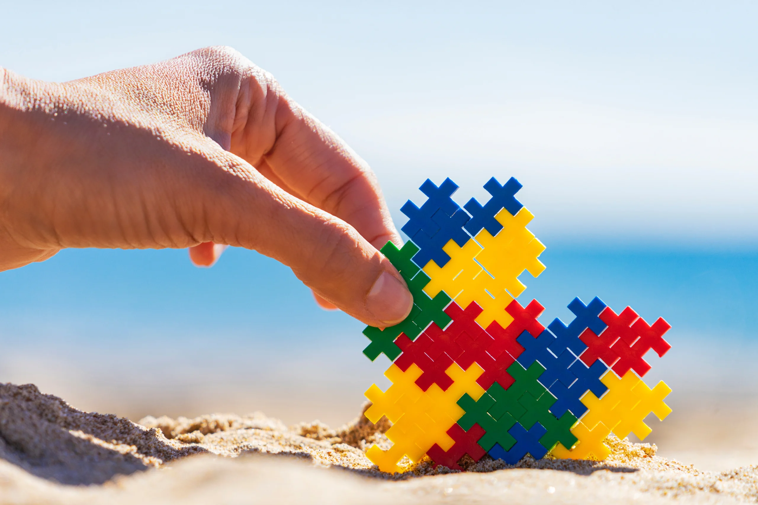Mano che compone un puzzle colorato sulla sabbia con il mare sullo sfondo